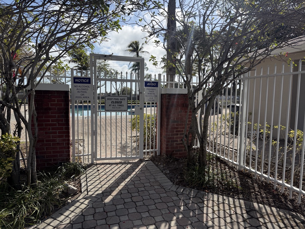 White metal pedestrian gate securing an HOA community pool area